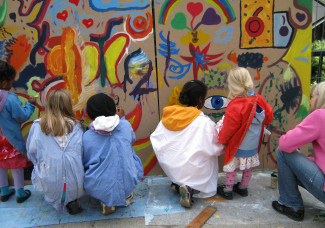 Kinder malen gemeinsam auf großer Holzplatte