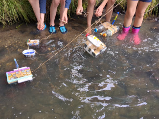 Kinder lassen selbstgebaute Boote im Fluss schwimmen