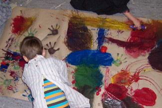 Kinder malen mit Malwerkzeugen auf großer Packpapierbahn auf dem Boden
